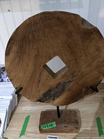 Wooden circular spool end showing natural grain and mounted on black metal rod with wooden base.