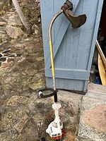 Full side view of the Stihl FS 38-Z trimmer showing the white body, curved metal shaft, handle, and cutting head with guard on stone floor next to a blue door.