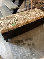 Overall view of storage bench showing zebra print upholstered top and black base.