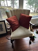 Front view of traditional beige accent chair with two rust-red cushions on it, wooden carved legs visible.
