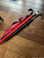 Three closed umbrellas lying on wooden flooring showing handles and part of shafts.