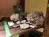 Overall display of nine mineral and rock specimens set on a wooden surface showing rough and polished textures with visible color variations