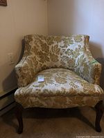 Full view of upholstered arm chair showing floral upholstery and wooden legs.
