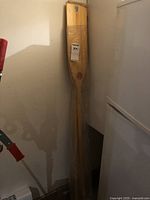 Pair of wooden paddles standing upright wrapped in plastic, showing overall length and shape.