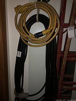 Two electric cables coiled and hanging on a wall. One cable is yellow, the other black. Both show signs of use with some dirt and minor wear.