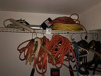 Multiple extension cords in various colors hanging on a metal wire shelf.