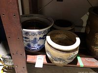 Three ceramic and brass planters on shelf, including blue and white ceramic piece and rustic ceramic pot