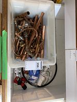 Plastic bin filled with multiple copper pipes and pipe fittings, pipe cutter tool, gloves, and bilge pump.