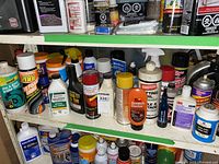 Shelf with multiple automotive maintenance liquids including tire foams, brake fluids, cleaners, and oils organized on two shelves