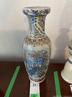 Front view of tall ceramic vase with blue floral and scenic painted design and gold overlay