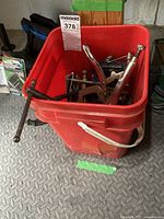 Red bucket filled with various locking clamps and C-clamps in assorted sizes.
