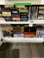 Photo showing two shelves with stacked VHS tapes and DVDs. Titles of VHS tapes visible include Titanic, Legend, Apollo 13, X-Men, Mrs. Doubtfire, Perfect Storm, Mission to Mars, Santa Claus among others.
