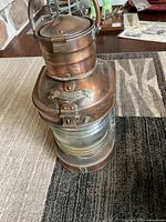 Full view of the copper ship lantern showing cylindrical body, glass lens, top chimney and handle.