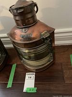 Copper ship's lantern sitting on floor with marked Port label, showing front and lens.