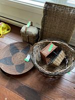 Multiple wicker decorative items placed on floor, including baskets, a large round tray with a dark floral/star pattern, and small containers