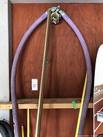 Windsurfing boom with purple padded grips and fiberglass mast leaning against wall.
