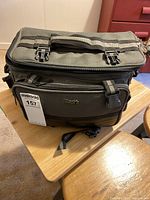 Closed MaxxTek green camera bag on wooden table showing carrying strap and compartments