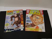 Photo showing two MAD magazines from 1999 and 2006, covers visible with distinct colorful cartoon illustrations and text