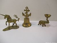 Front and side views of all three brass pieces: bell with anchor, unicorn on base, and elephant holding small bowl.