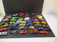 Wide view of assorted die cast cars arranged in rows on a black surface, showing various models and colors.