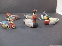 Set of six Avon duck figurines arranged on a black surface showing various duck species with detailed color patterns.