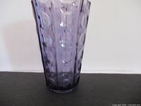 Front view of amethyst glass vase on black surface against white wall.