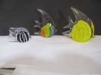 Wide shot of three art glass fish figurines arranged side by side on white surface with dark background, showing size and color differences.