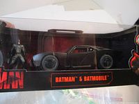 Front view of the boxed Batman figure and Batmobile, showing the figure standing next to the vehicle inside the packaging.