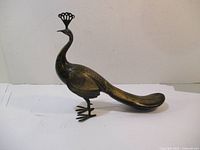 Side view of brass peacock figurine showing detailed side feathers and clawed feet.