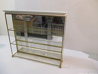 Front angled view showing brass frame, glass shelves, and mirrored back with etched design.