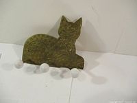 Front view of brass cat-shaped coat hook with three white ceramic knobs mounted as hooks