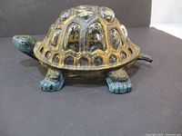 Photo showing side profile of cast iron turtle candle holder with detailed legs and head, glossy shell with gold and black patterns.