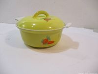 Round yellow enameled cast iron pot with vegetable art on body and lid, placed with lid on.