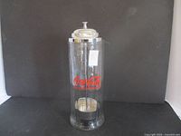 Front view of clear cylindrical straw dispenser with red Coca Cola logo and chrome lid.