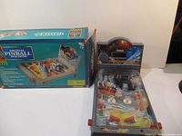 Digital table-top pinball machine displayed outside its original box, showing the full playfield and backboard display with s core lights and controls.