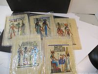 Five colorful Egyptian papyrus art sheets laid out grouped with visible detailed figures and hieroglyphs.