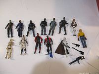 13 action figures from GI Joe and Star Wars including weapons and accessories displayed on white background.