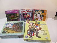Five boxed jigsaw puzzles arranged in a row on a table showing front covers with various artwork and puzzle piece counts of 1000 each.