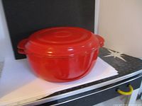 Red cast iron pot with lid on, showing side handles and glossy red exterior.