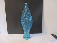 Front view of the blue glass fish-shaped bottle against a black background.