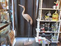 Full-height view of gray metal heron on rectangular base amid store fixtures