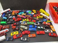 Overview of multiple toy cars and trucks in various colors including red, yellow, blue, green, and black, arranged on a black surface.