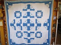 Full view of the blue and white patchwork quilt hanging, showing its overall pattern and border.