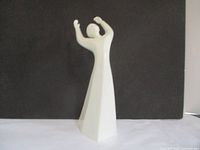 White ceramic figure of a person with arms raised, shown from rear against a black background.