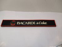 Front view of the 24-inch rubber bar mat with Bacardi & Coke branding on black background with red trim.