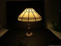 Lit Tiffany style lamp showing cream stained glass shade and decorative band.
