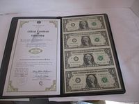 Front view of the black folder containing the uncut sheet of four $1 bills on the right and the official certificate of ownership on the left.