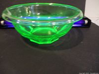 Side angle view of the translucent green uranium glass bowl showing geometric facets and smooth rim.