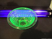 Green uranium glass bowl glowing brightly under UV light, showing internal pattern and smooth rim.