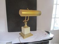 Front view of vintage desk lamp showing brass cylindrical shade, white marble base, and brass detailing on ornate bottom platform.